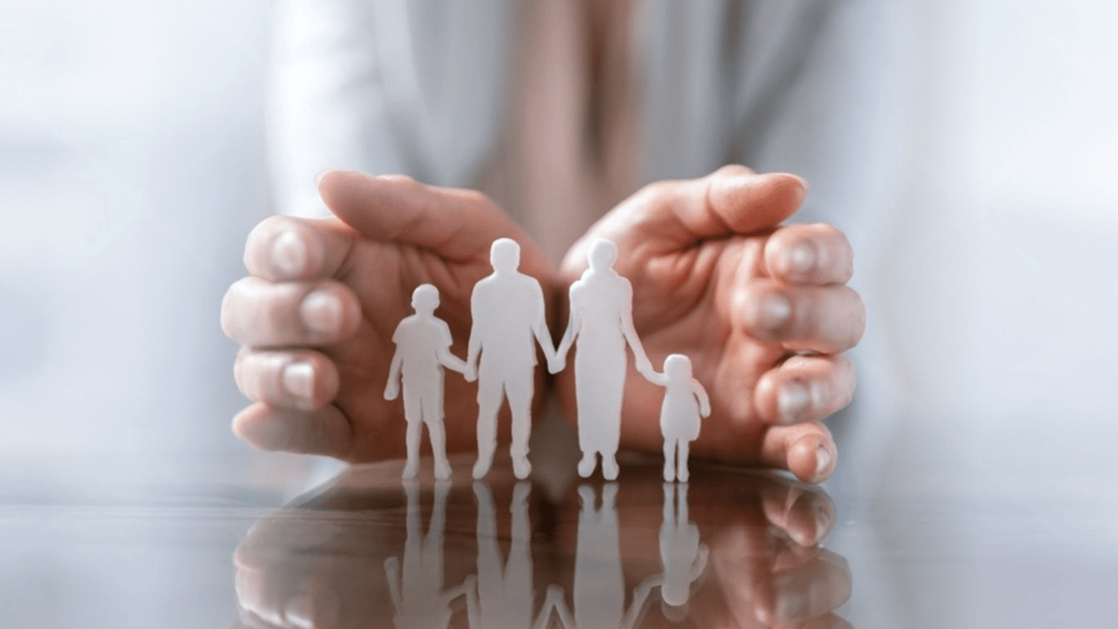 Hands gently shielding paper cut-out figures of a family, symbolising safeguarding children and vulnerable adults.